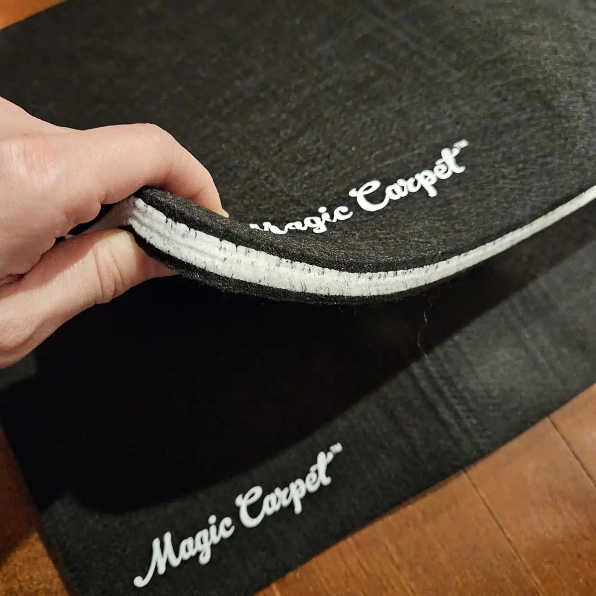 Close-up of a hand holding a black Magic Carpet mat showing its absorbent layered construction