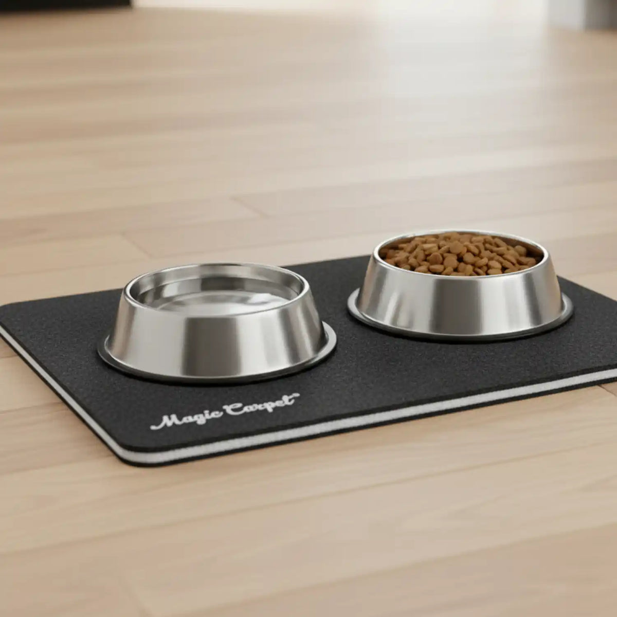 Two stainless steel pet bowls with food and water on a black Magic Carpet feeding mat